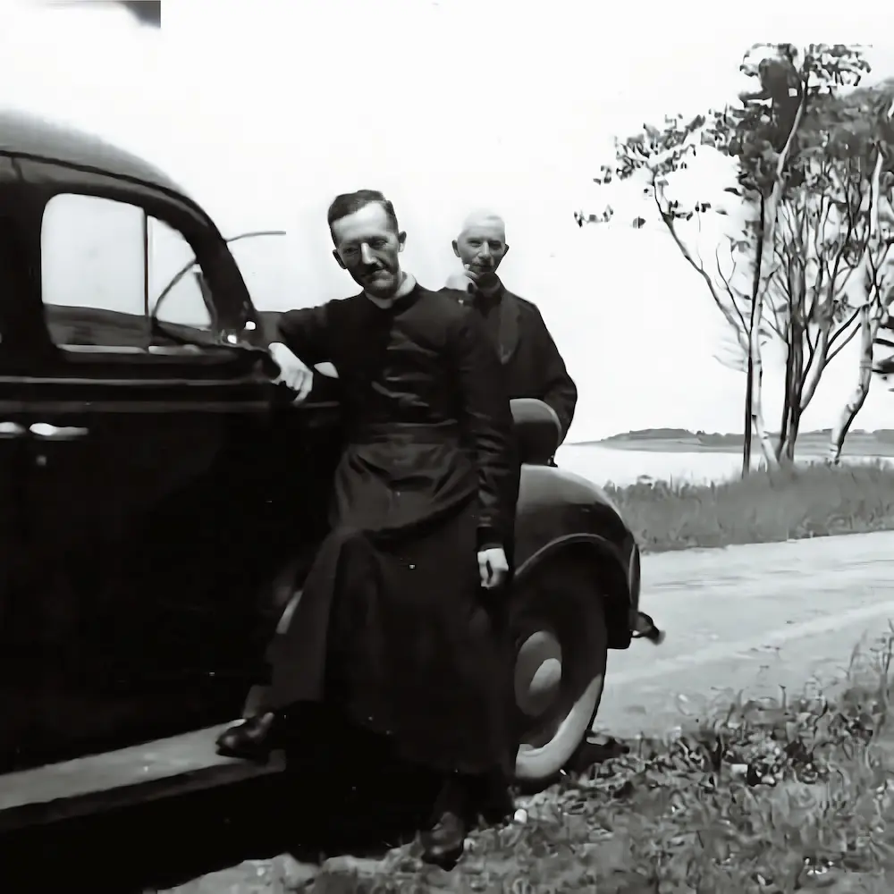 Father Basile Babin and a fellow priest beside a vintage car
